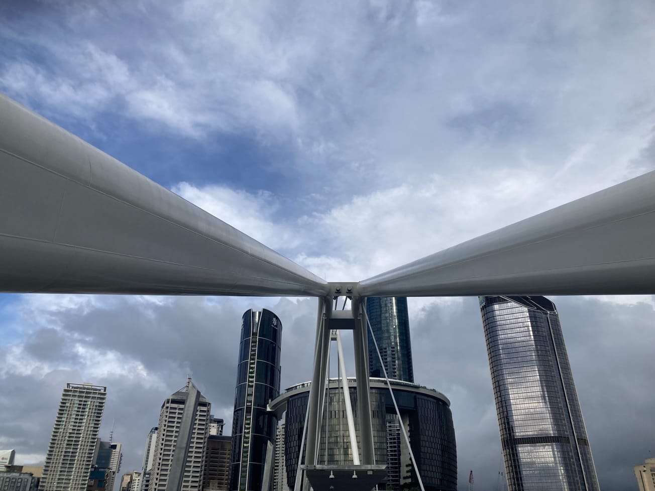 Two poles of a bridge stretching towards the centre of the image with a city landscape behind